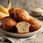 Freshly baked Air Fryer Banana Muffins on a plate with one cut open to reveal a moist, fluffy texture